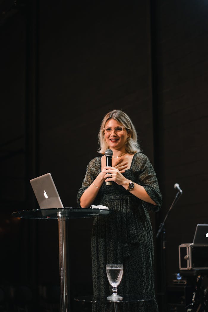 services-02 A woman giving a presentation on stage with a microphone and laptop.