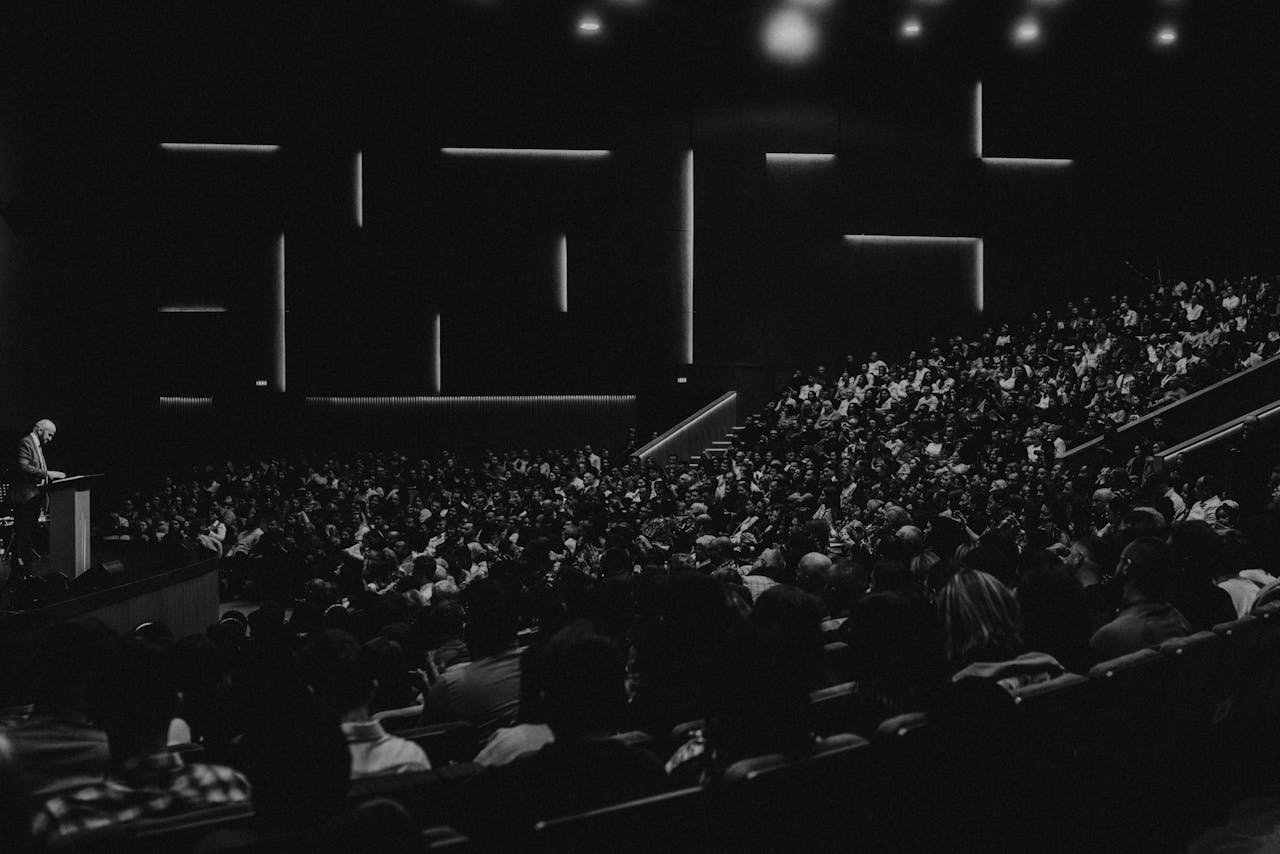 about-us Black and white photo of a large audience in an auditorium with a speaker at the lectern in Oradea.